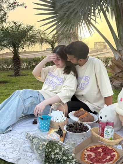 Two people enjoying a picnic in a park with food and drinks on a blanket.